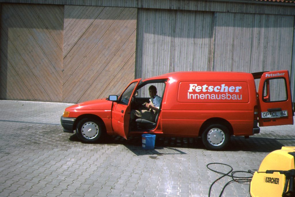 Rotes Fahrzeug mit der Aufschrift Fetscher Innenausbau, eine Person sitzt am Steuer