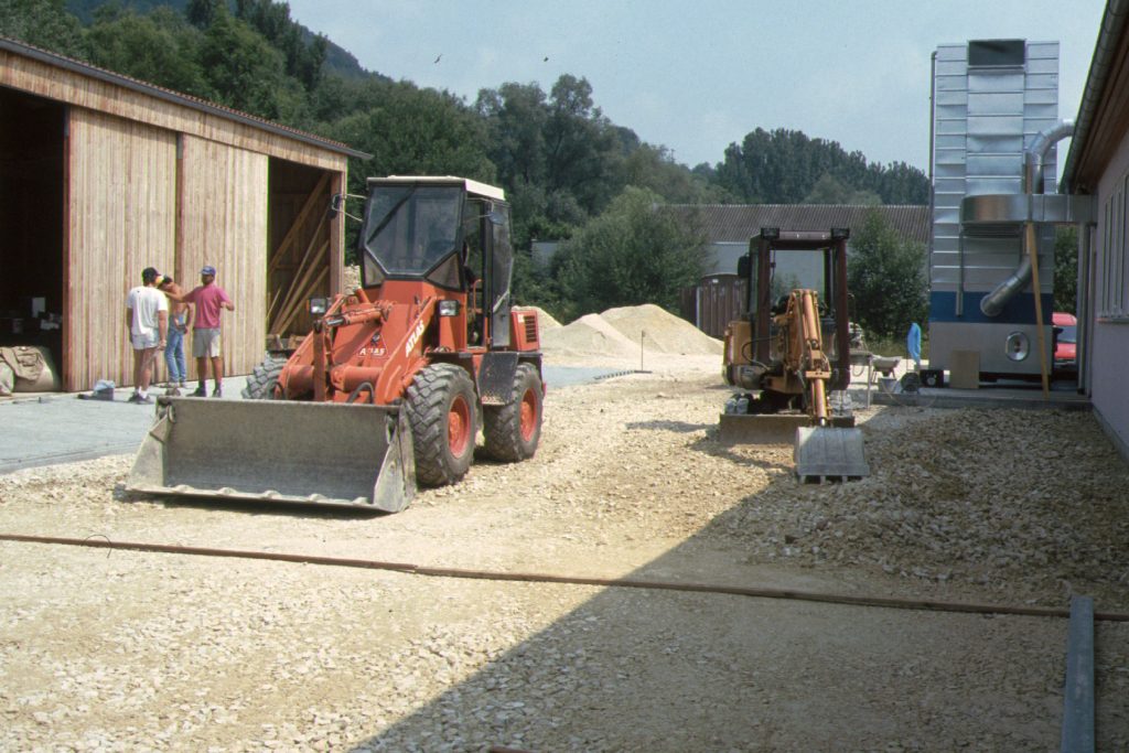 zwei Bagger stehen im Kies neben einer Halle
