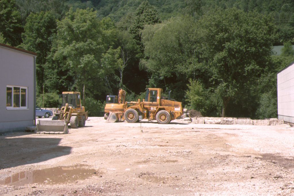 Drei gelbe Baustellenfahrzeuge stehen auf einer Baustelle im Kies