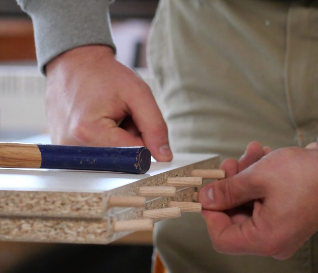 Dübel werden in eine Holzplatte gesteckt